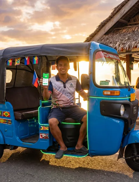 A Siquijor Go tricycle driver holding the app at sunset